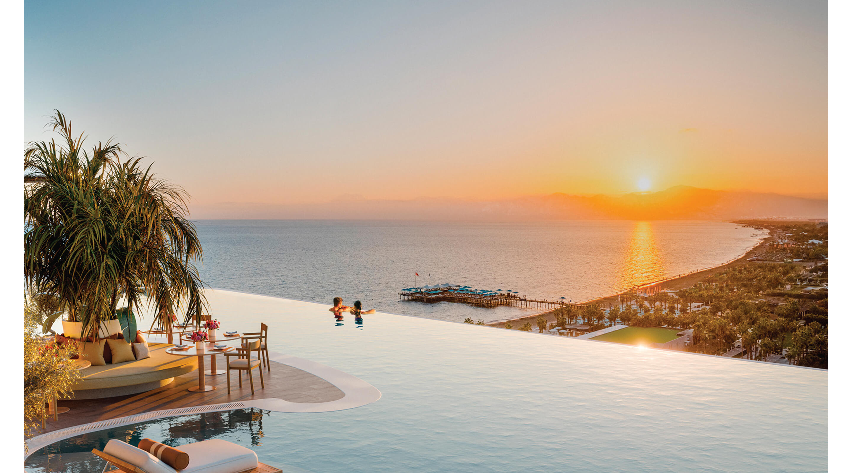 Rooftop infinity pool overlooking the sea and coastline at sunset.